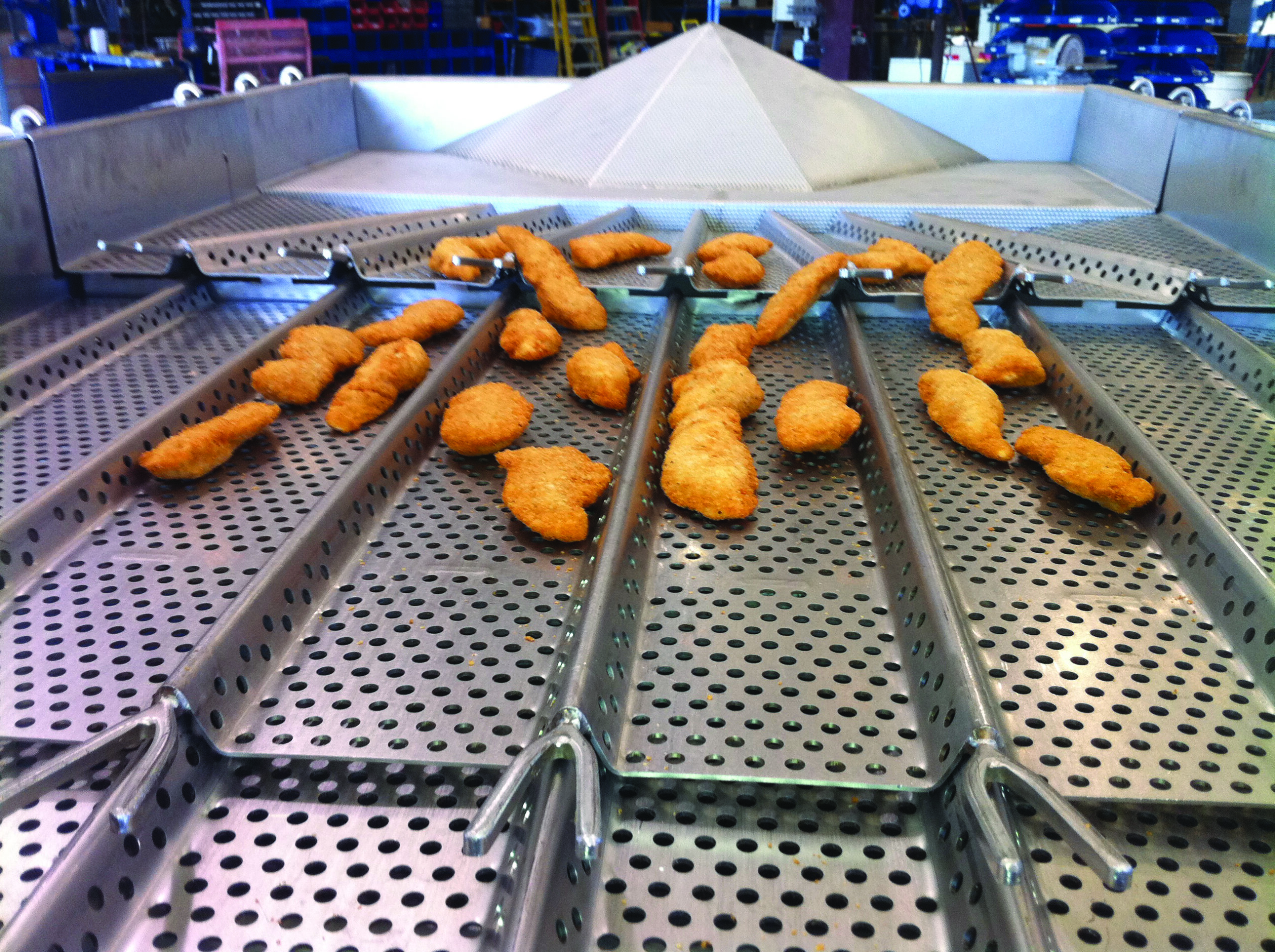 A PFI laning vibratory conveyor moving processed chicken nuggets.